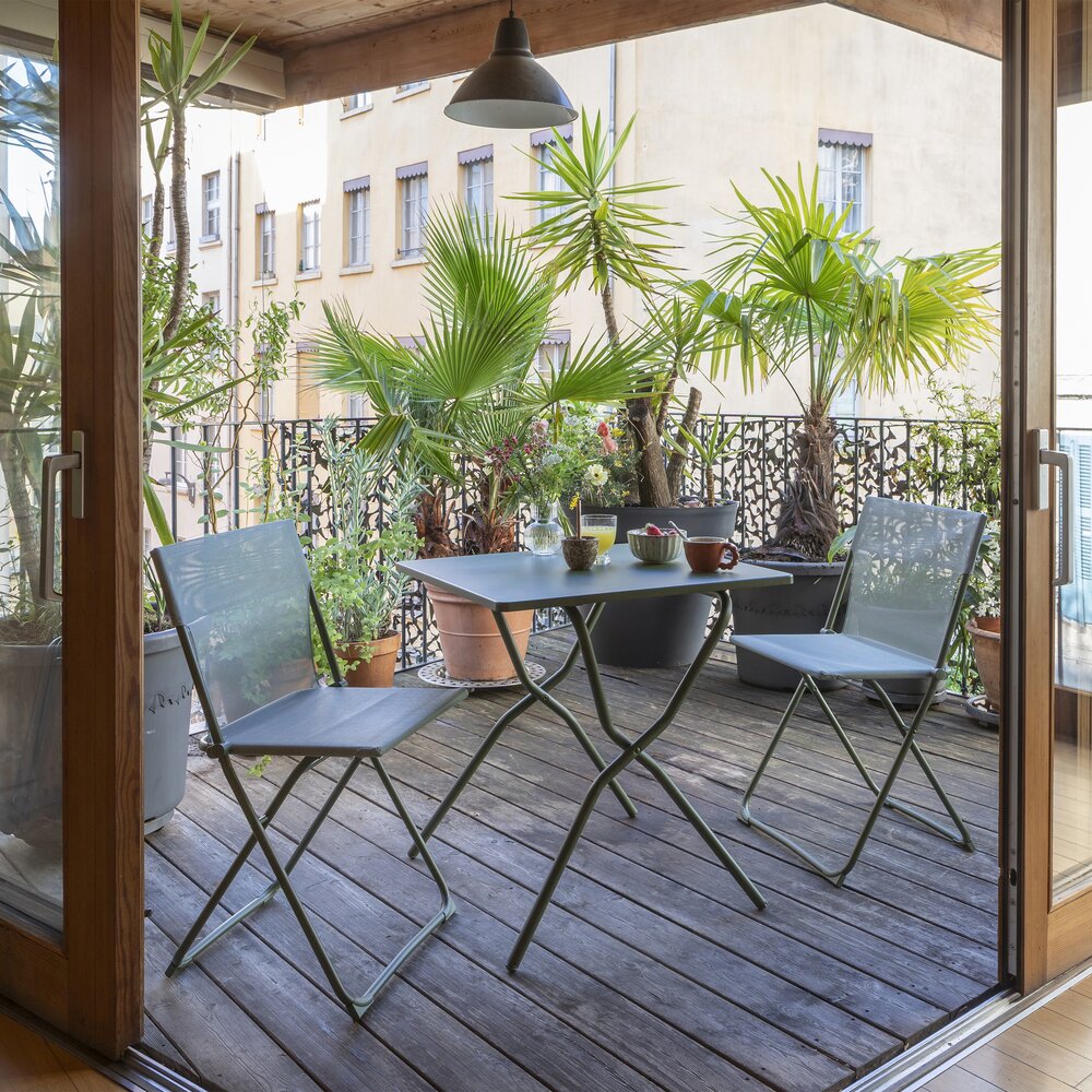 A small outdoor dining set consisting of a square metal table and two folding chairs on a wooden decked balcony