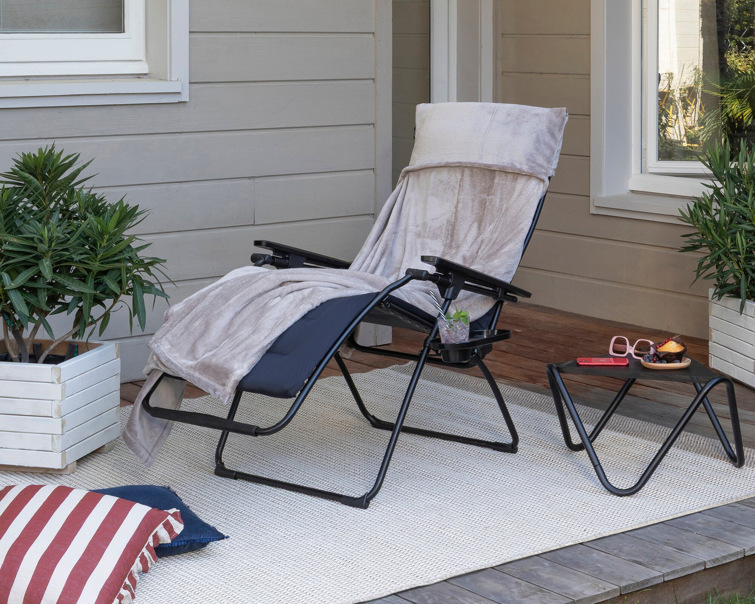 A black outdoor zero gravity chair with a beige throw blanket draped over it, set on a porch
